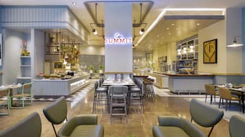 A modern cafe with a central seating area, a bar, and a variety of food displays.