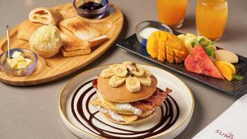 A breakfast plate with pancakes, bacon, and bananas, accompanied by toast, butter, and a fruit plate.