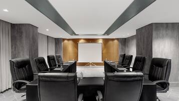 A conference room with a long table, black leather chairs, a projector screen, and a modern ceiling design.