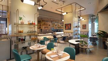 Un interior de restaurante moderno con sillas color turquesa, mesas redondas y una variedad de platos exhibidos en estanterías.