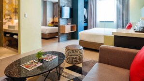 Una habitación de hotel moderna con una cama, un escritorio, un televisor y un baño visible a través de una puerta abierta.