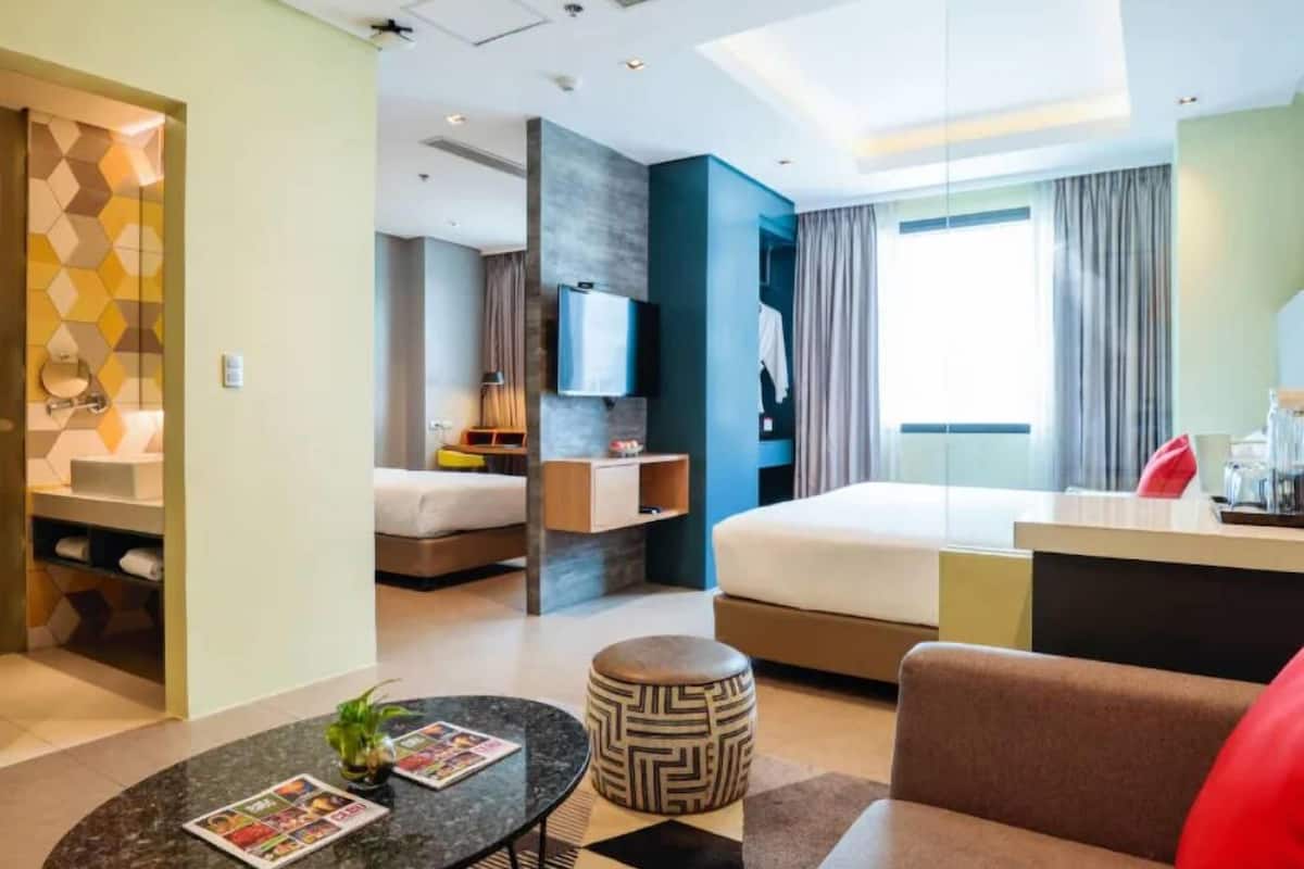 A modern hotel room with a bed, a desk, a TV, and a bathroom visible through an open door.