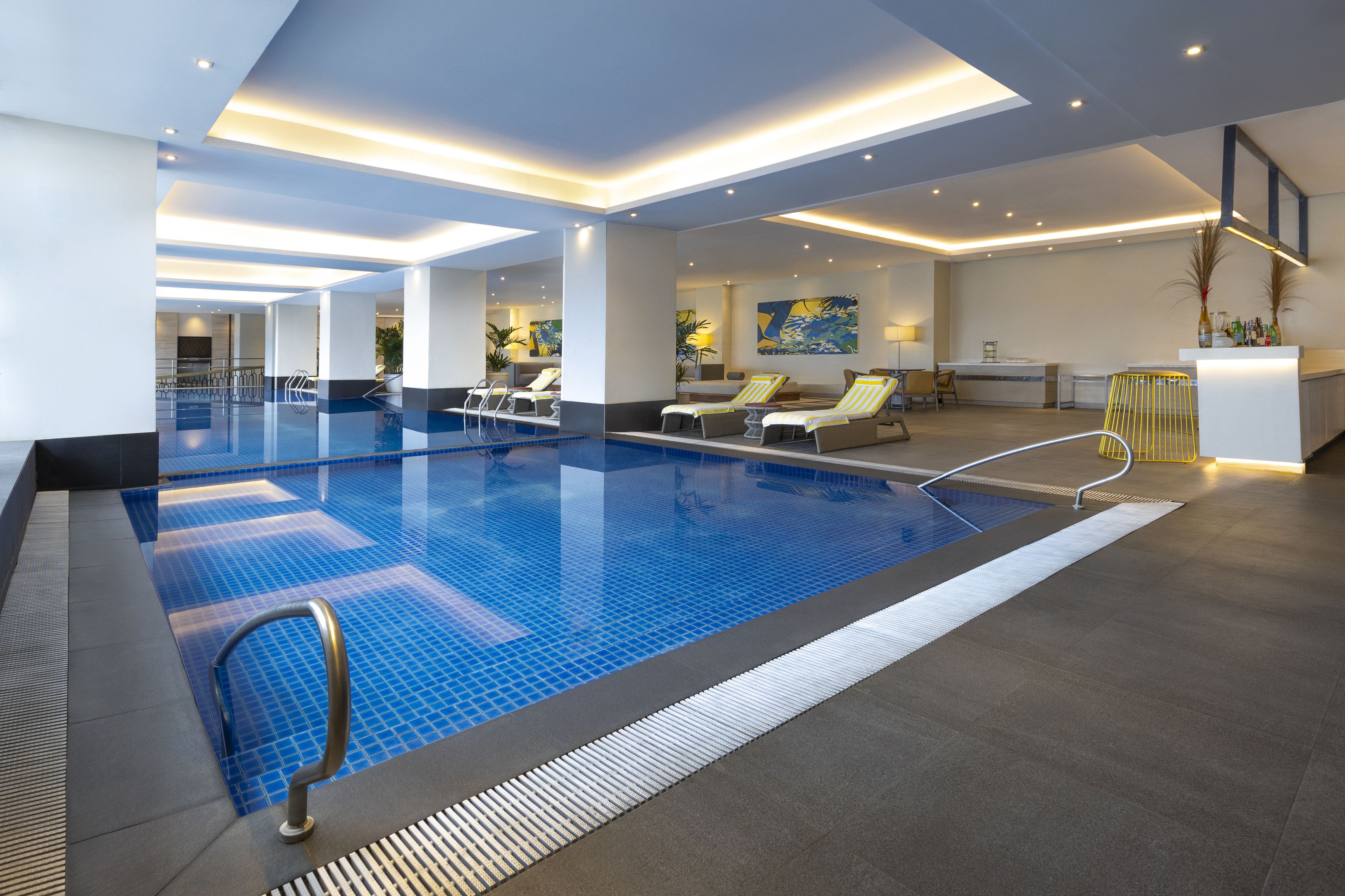 Una piscina interior moderna con sillones de descanso, una zona de recepción y un bar.