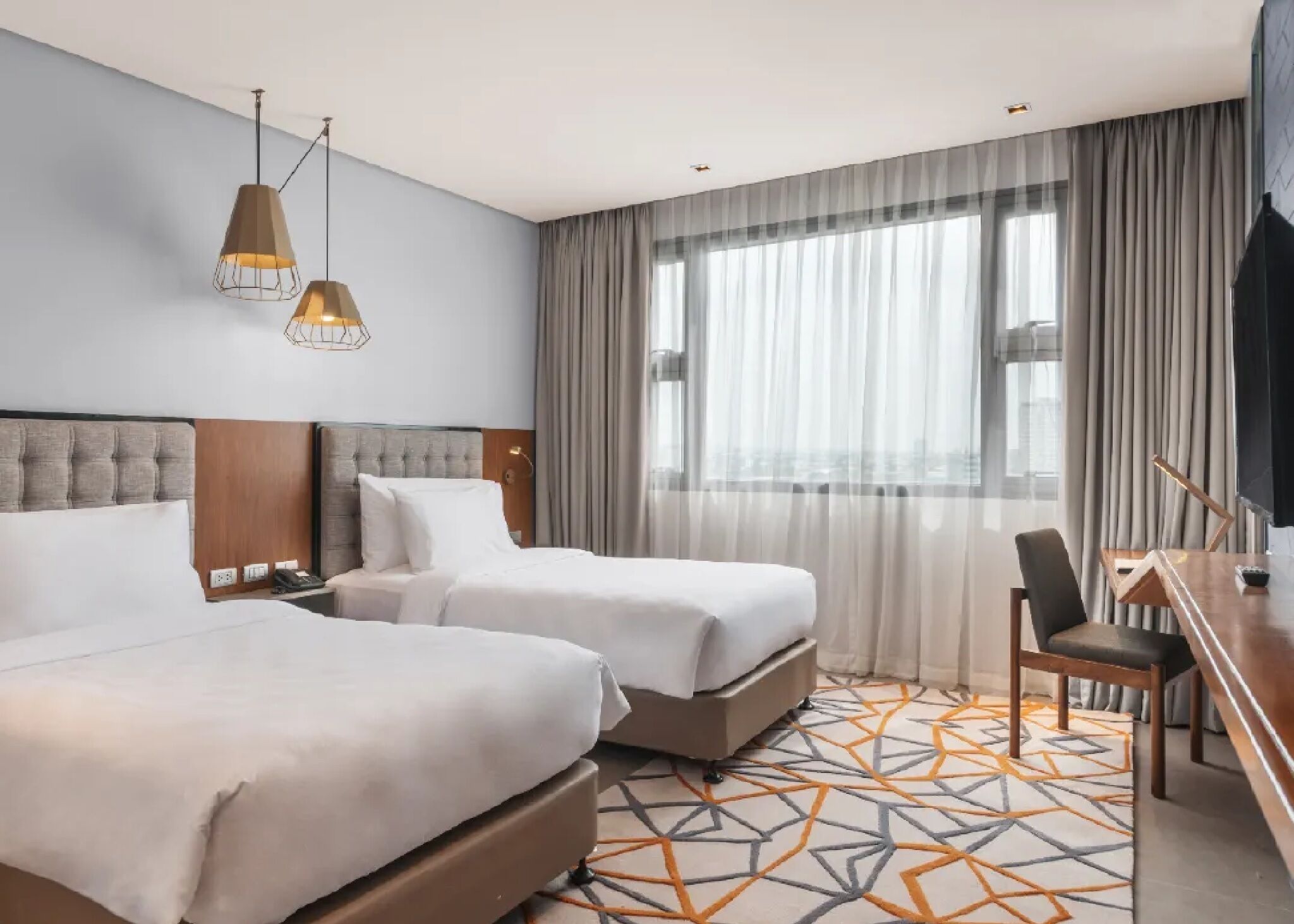 A hotel room with two beds, a desk, and a chair.