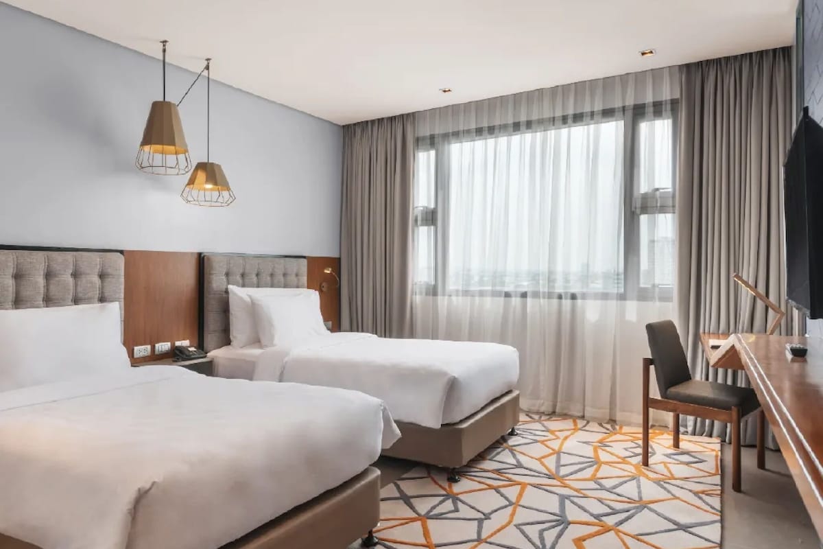 A hotel room with two beds, a desk, and a chair.