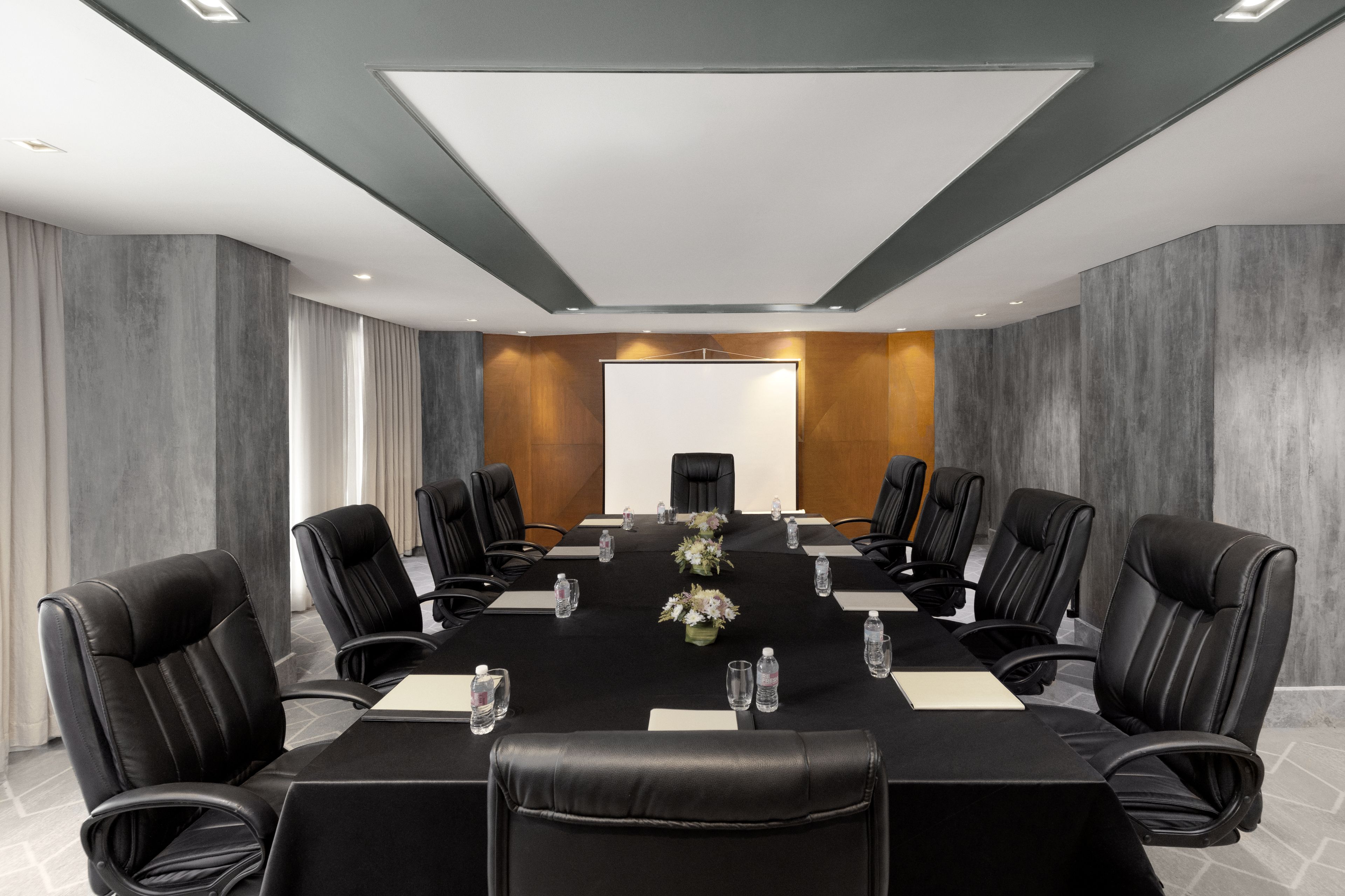 A conference room with a long table, black leather chairs, and a whiteboard at the front.