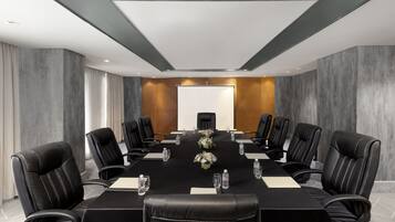 A conference room with a long table, black leather chairs, and a whiteboard at the front.