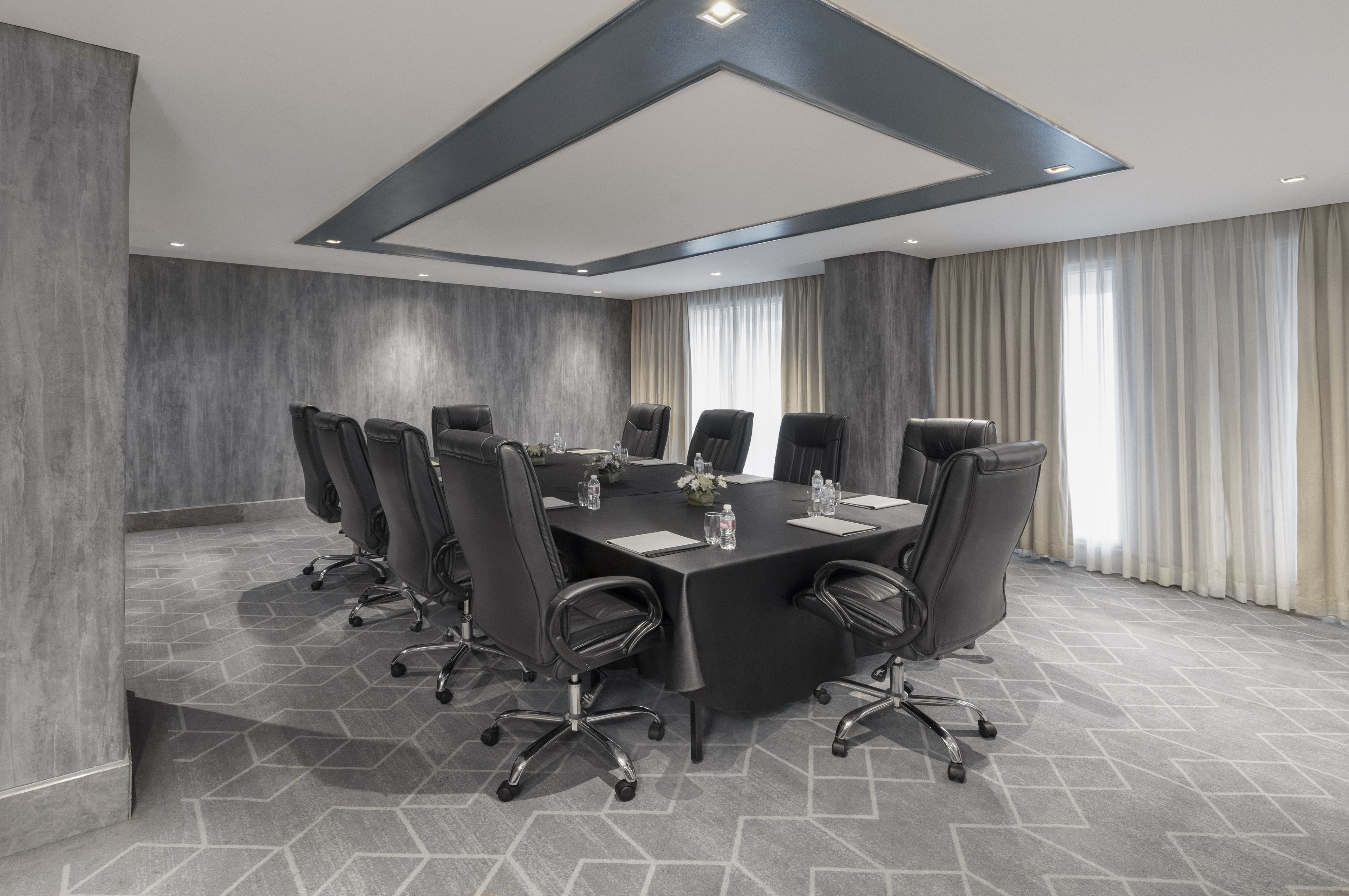 A conference room with a large rectangular table, multiple chairs, and a modern ceiling design.