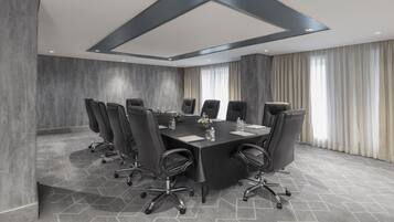 A conference room with a large rectangular table, multiple chairs, and a modern ceiling design.