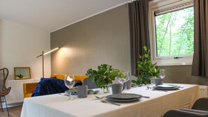 A dining table set with plates, glasses, and cutlery, a vase with greenery, and a window with curtains.