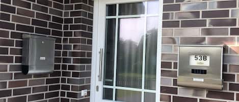 A white door with a glass panel, a mailbox, and a mail slot on a brick wall.