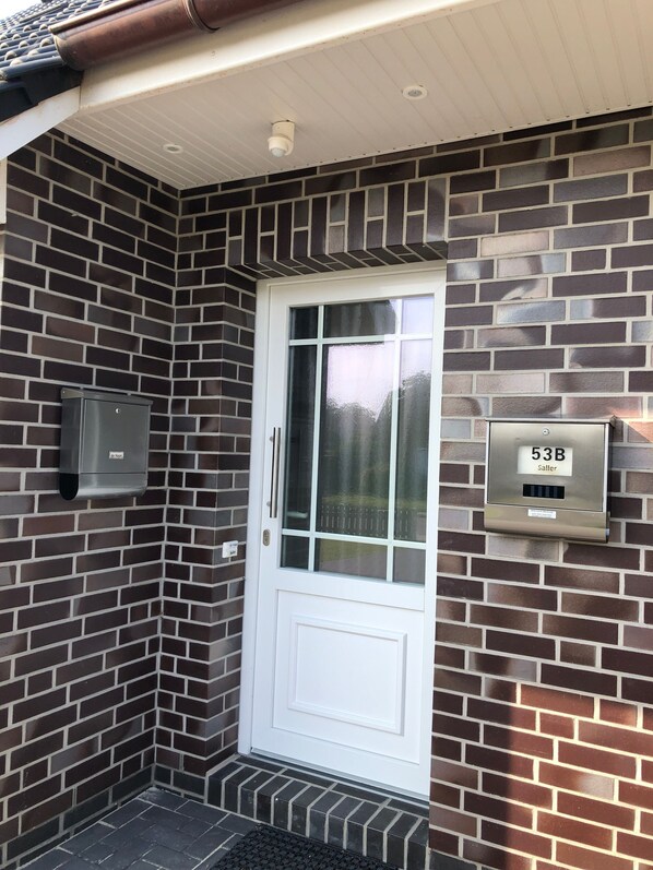 A white door with a glass panel, a mailbox, and a mail slot on a brick wall.