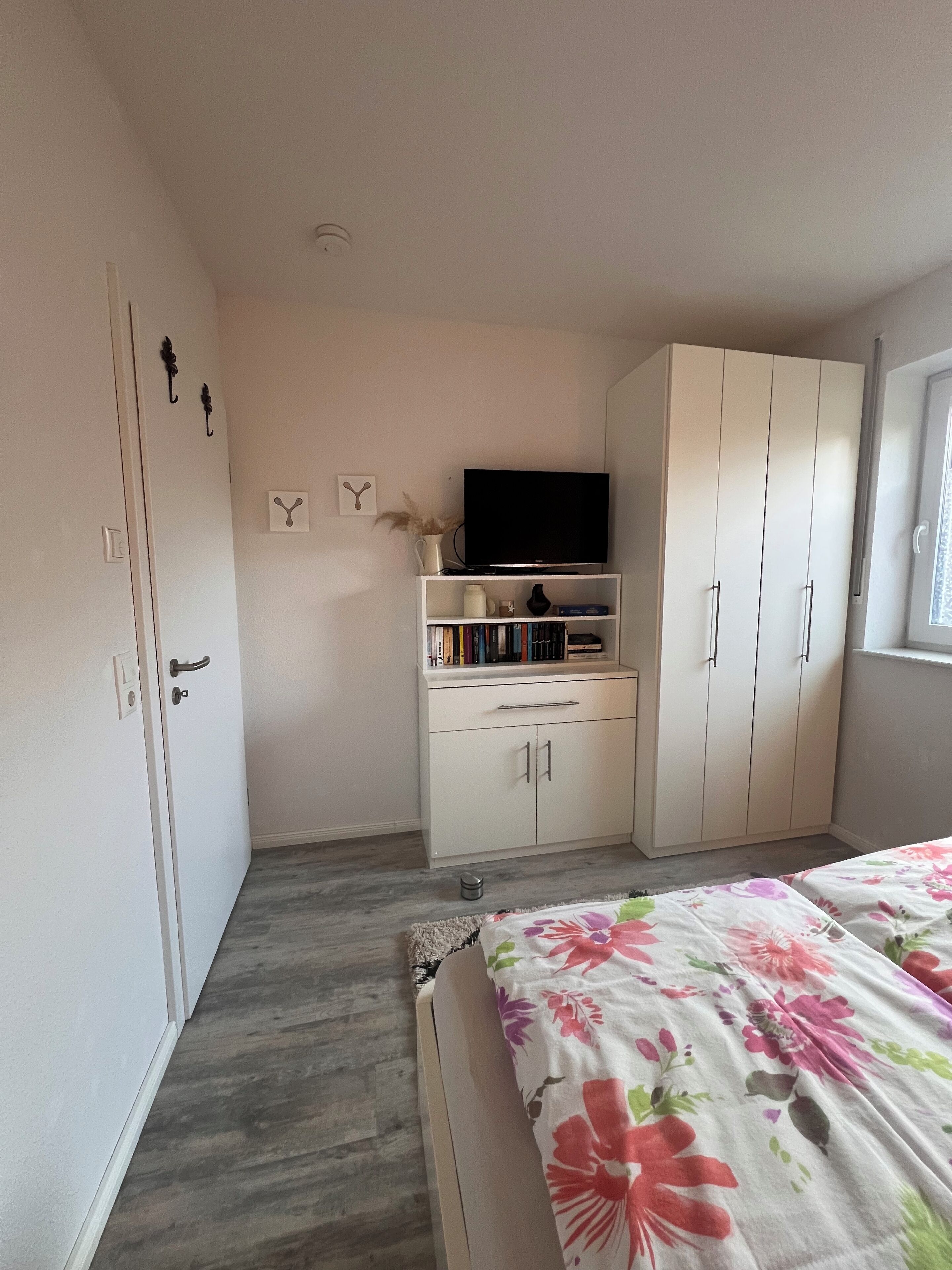Ein Schlafzimmer mit einem Bett, einem Fernseher auf einem Regal, einem Kleiderschrank und einem Fenster.
