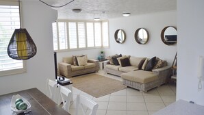 Una sala de estar con dos sofás, una mesa de centro y una mesa de comedor con sillas. Hay tres espejos colocados en la pared y una lámpara colgante.