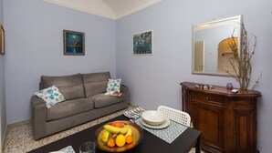 A living room with a sofa, a dining table with a fruit bowl, and a cabinet. - Accogliente (Roma)