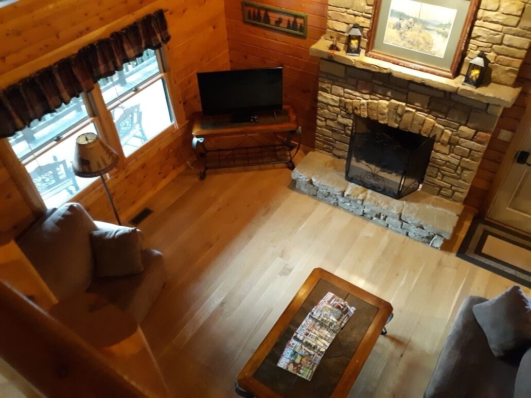 A cozy log cabin interior with a stone fireplace, wooden furniture, and a television on a stand.