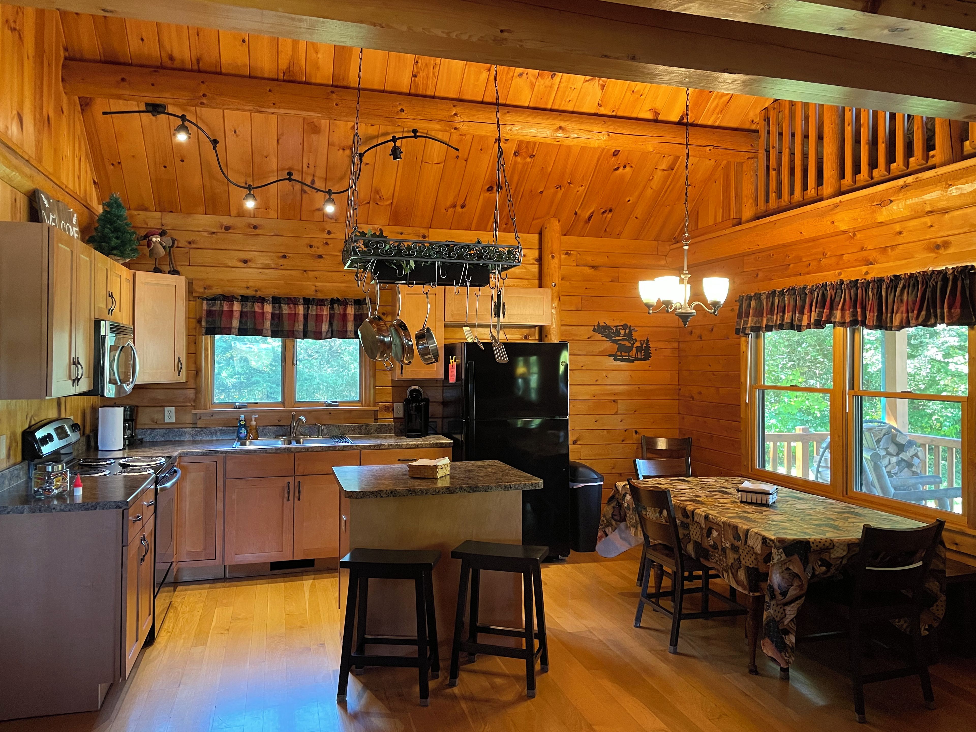 A cabin interior with a kitchen, dining area, and a large window offering a view of the outdoors.
