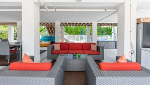 Ein moderner Außenbereich mit einer roten Couch, grau-orangenen Kissen und einem Couchtisch mit Glasplatte.