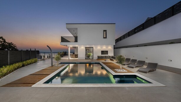 Ein modernes, zweistöckiges Haus mit Schwimmbad, Sitzgelegenheiten im Freien und Meerblick.