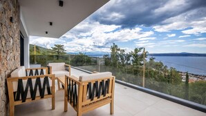 Ein Balkon mit zwei Holzstühlen und einem Tisch, der einen schönen Blick auf ein Gewässer und sanfte Hügel bietet.