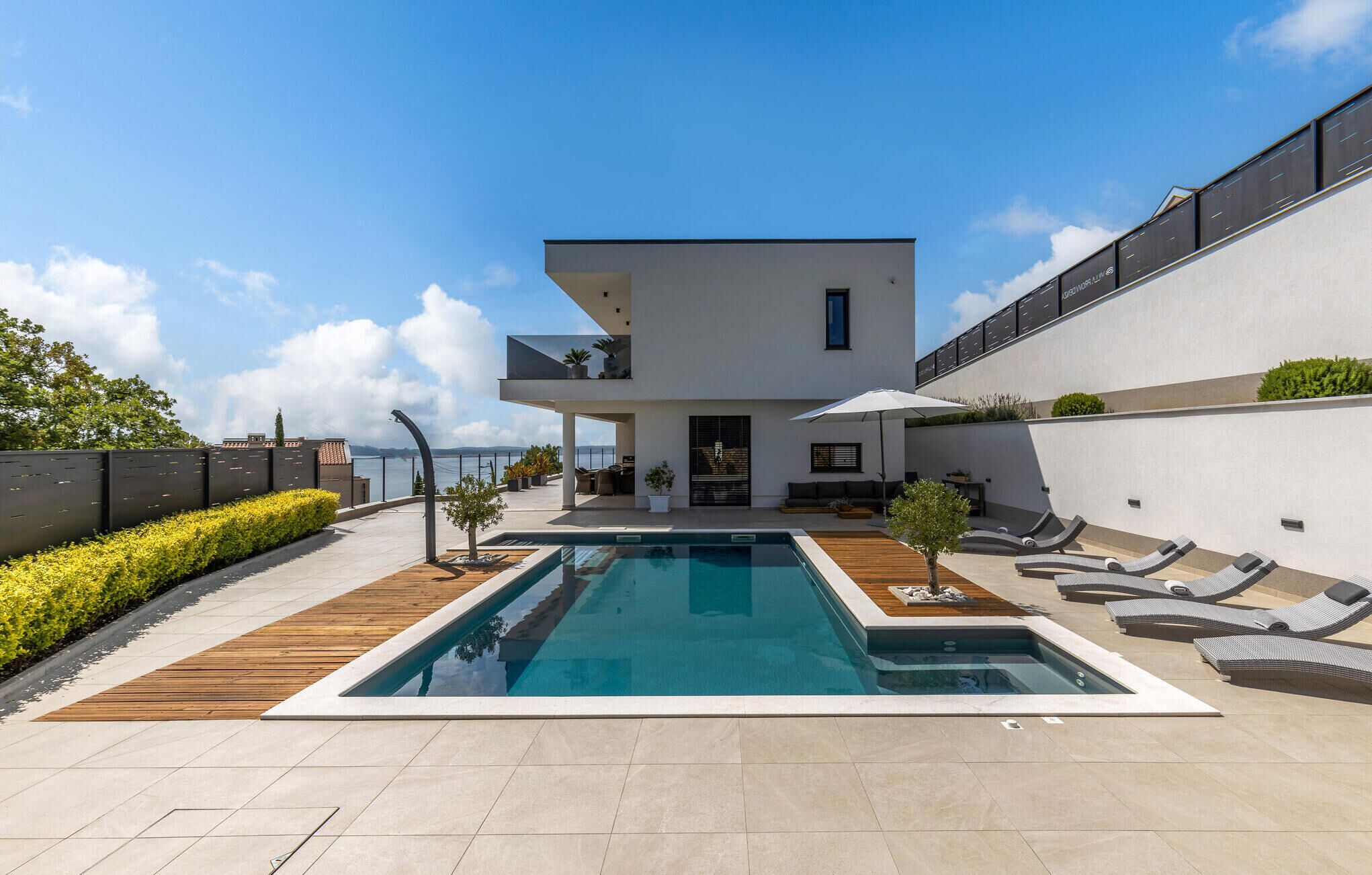 A modern house with a pool, outdoor seating, and a view of the sea.