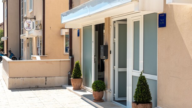 L’entrée d’un hôtel, avec une porte en verre, une enseigne et des plantes en pot.