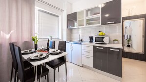 Une cuisine moderne avec des meubles blancs et gris, une table à manger pour quatre personnes et une fenêtre équipée de stores.
