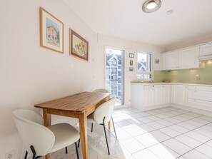 Une cuisine moderne avec des meubles blancs, une table à manger en bois et deux chaises blanches.