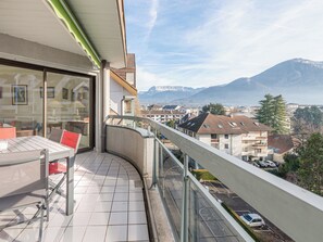Un balcón con vistas a una cadena montañosa, suelo de baldosas y una mesa con sillas.