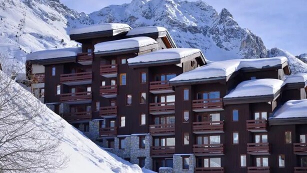 A cluster of multi-story buildings with balconies, set against a backdrop of snow-covered mountains. - At the foot of the Slopes (La Plagne-Tarentaise)