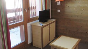 A small room with a wooden desk, a television, a lamp, and a window with curtains. - At the foot of the Slopes (La Plagne-Tarentaise)