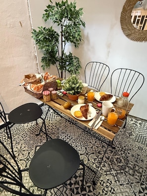 A breakfast setup with a wooden table, two chairs, a potted plant, and a tiled floor.