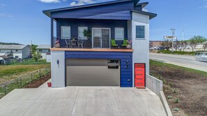 Un bâtiment moderne à deux étages, doté d’un garage, d’un balcon avec mobilier d’extérieur et surplombant un ciel dégagé.