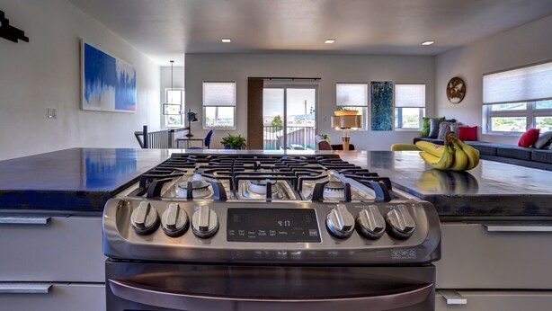 Une cuisine moderne dotée d’une cuisinière en acier inoxydable, d’un grand îlot central et offrant une vue sur l’extérieur.