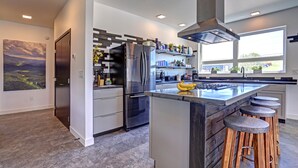 Une cuisine moderne dotée d’un grand îlot central, d’appareils électroménagers en acier inoxydable et offrant une vue sur l’extérieur.