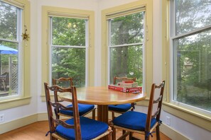A dining area with a round table, four wooden chairs with blue cushions, and a Monopoly board game.