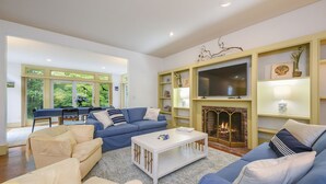 Amplia sala de estar con chimenea, televisor y comedor con ventanas grandes.
