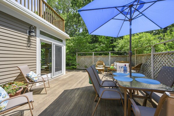 An outdoor deck with a table and chairs, a blue umbrella, and a wooden fence.