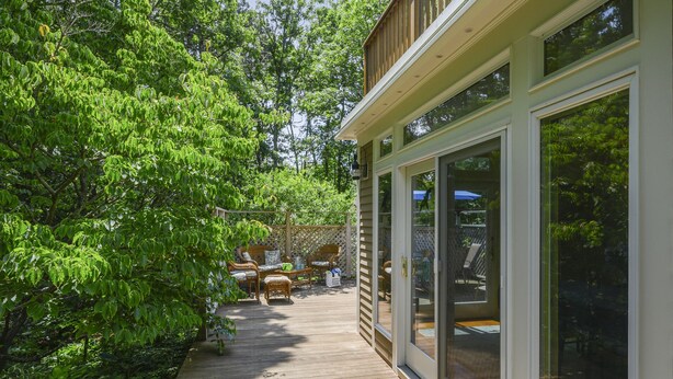 Un patio cubierto con mobiliario exterior, una terraza de madera y una sala con paredes de vidrio.