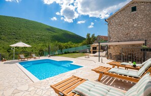 Relax by the serene pool surrounded by lush green hills and comfortable lounge chairs.