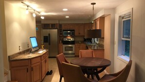 Eine Küche mit Essbereich, ausgestattet mit Kühlschrank, Backofen, Mikrowelle und einem Computer auf der Arbeitsfläche.