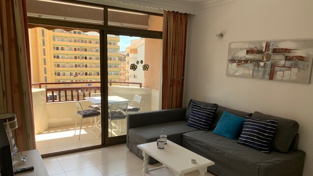 Ein Wohnzimmer mit grauem Sofa, einem weißen Couchtisch und einem Balkon mit Tisch und Stühlen.