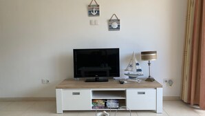 Ein Wohnzimmer mit Flachbildfernseher auf Holz-TV-Möbel, einer kleinen Segelboot-Dekoration und einer Lampe.