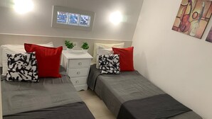 Ein Doppelzimmer mit zwei Betten, einem kleinen weißen Schminktisch, einer Deckenleuchte und einem an der Wand hängenden Bild.
