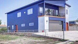 A modern two-story house with a blue exterior, a balcony on the upper floor, and a garage.