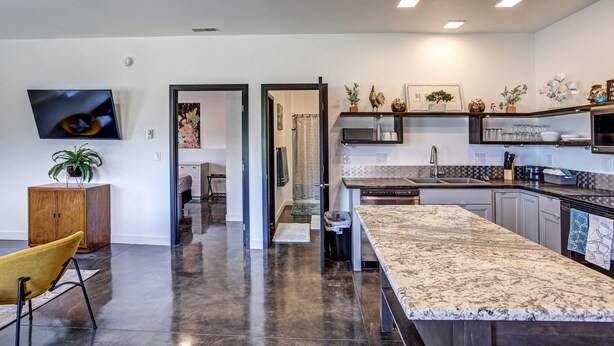 A modern kitchen with a granite countertop, built-in appliances, and a flat-screen TV.