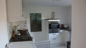 Une cuisine compacte équipée d’un réfrigérateur, d’un four et d’un four à micro-ondes. Un tableau est accroché au mur et une machine à café est posée sur le plan de travail.