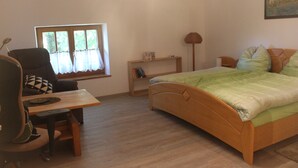 Une chambre à coucher avec un lit en bois, un bureau avec une chaise, une fenêtre avec des rideaux et une petite table de chevet.