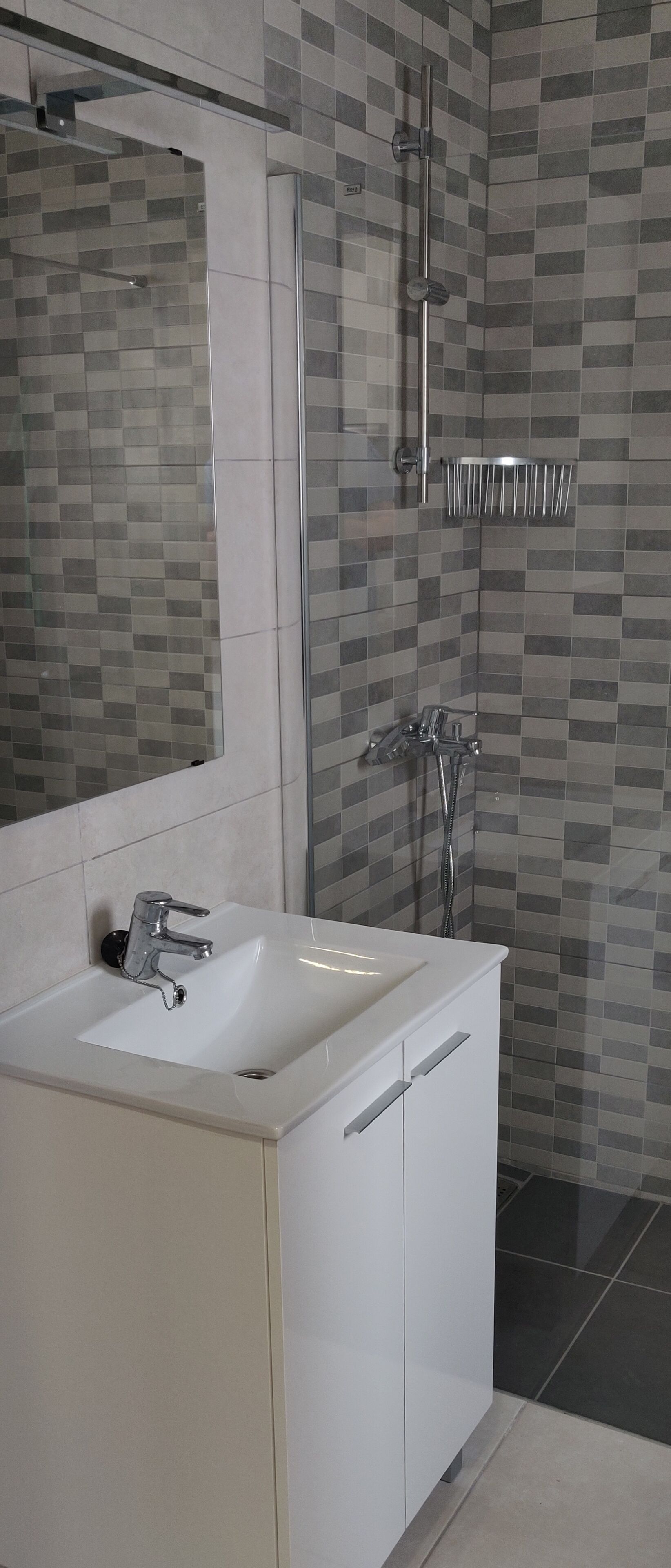 A modern bathroom with a white sink, a glass shower enclosure, and a tiled shower wall.