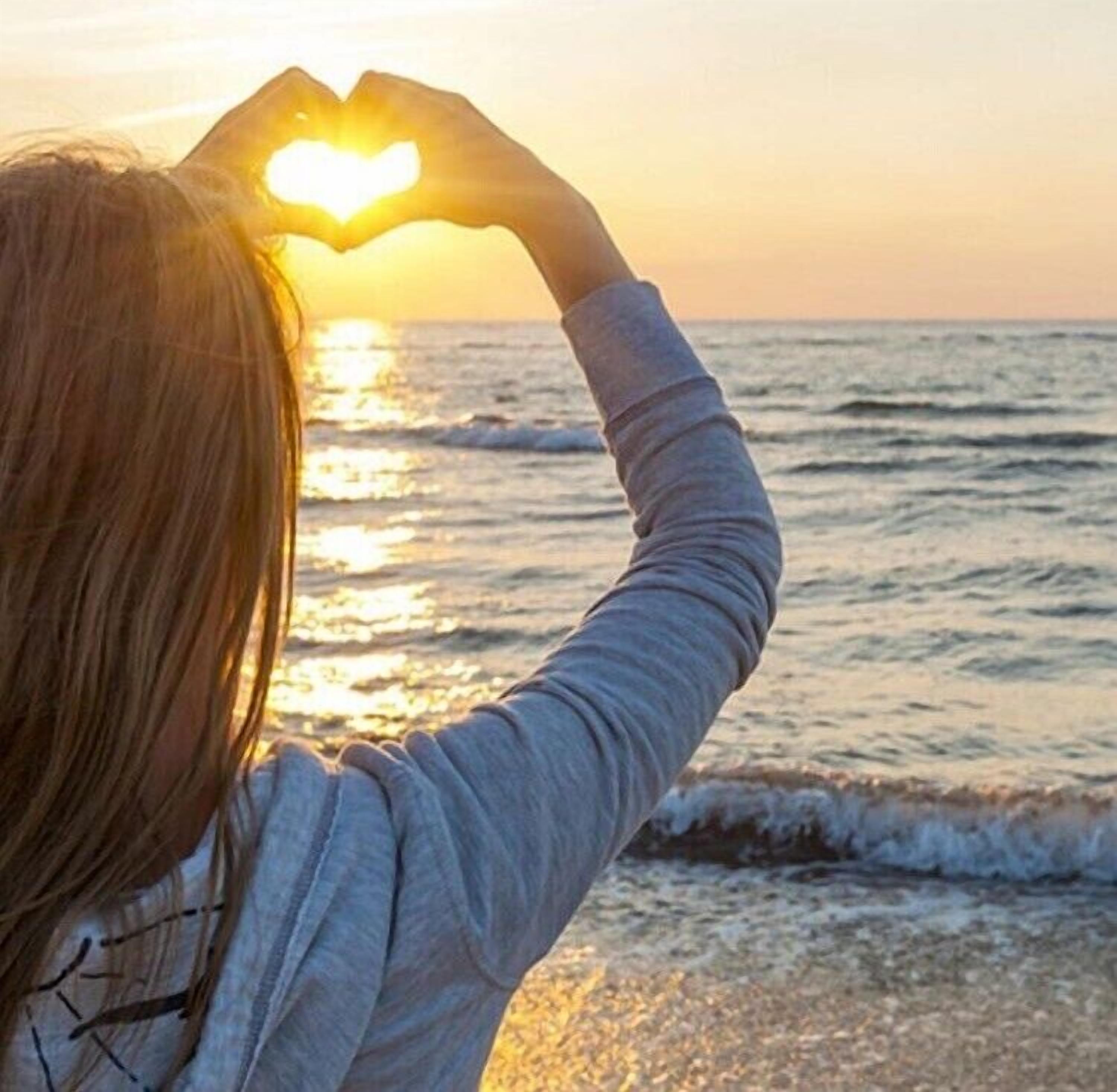 Una persona forma un corazón con las manos al atardecer sobre el océano.